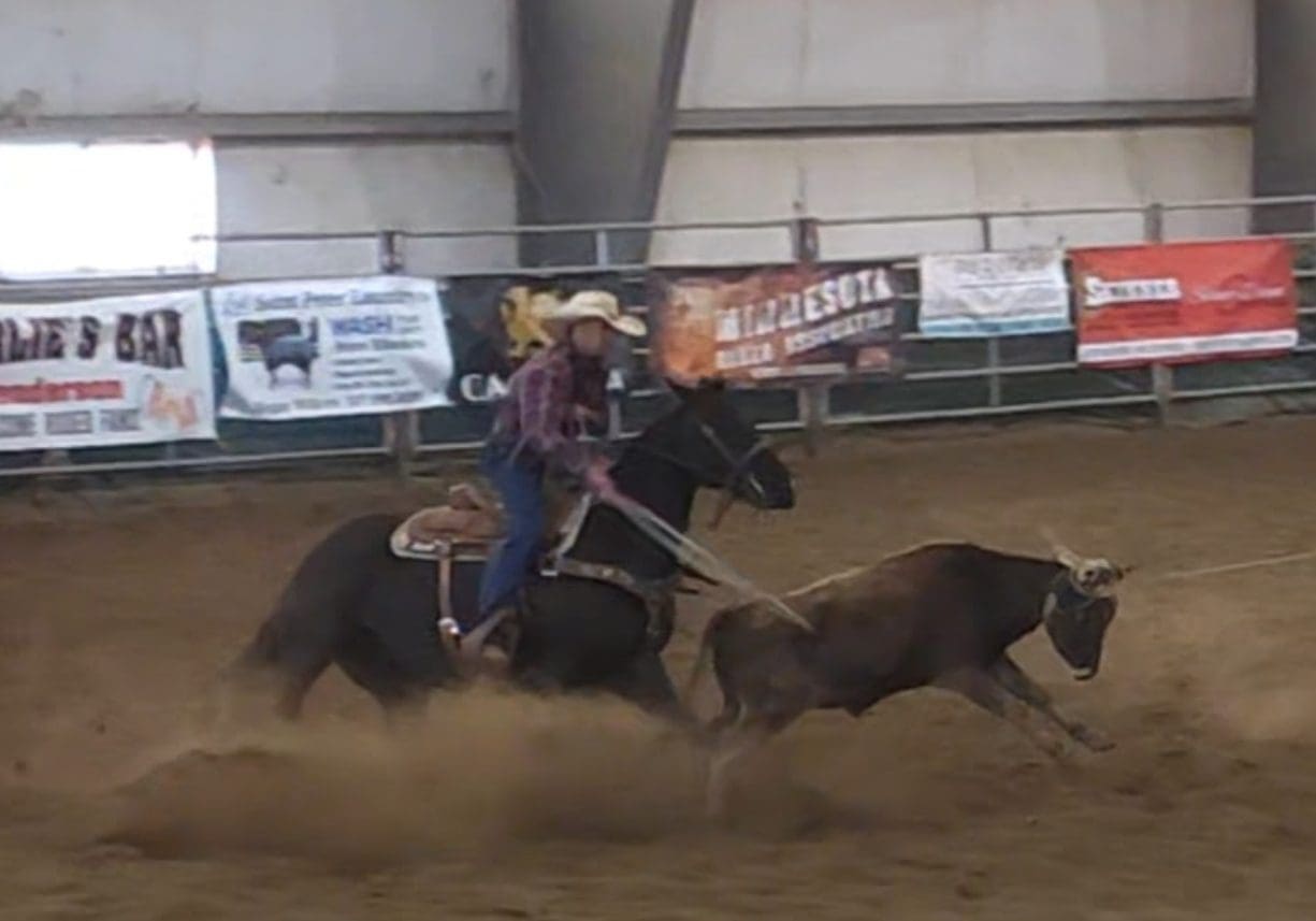 A rider on horseback chasing a calf in a dusty rodeo arena.